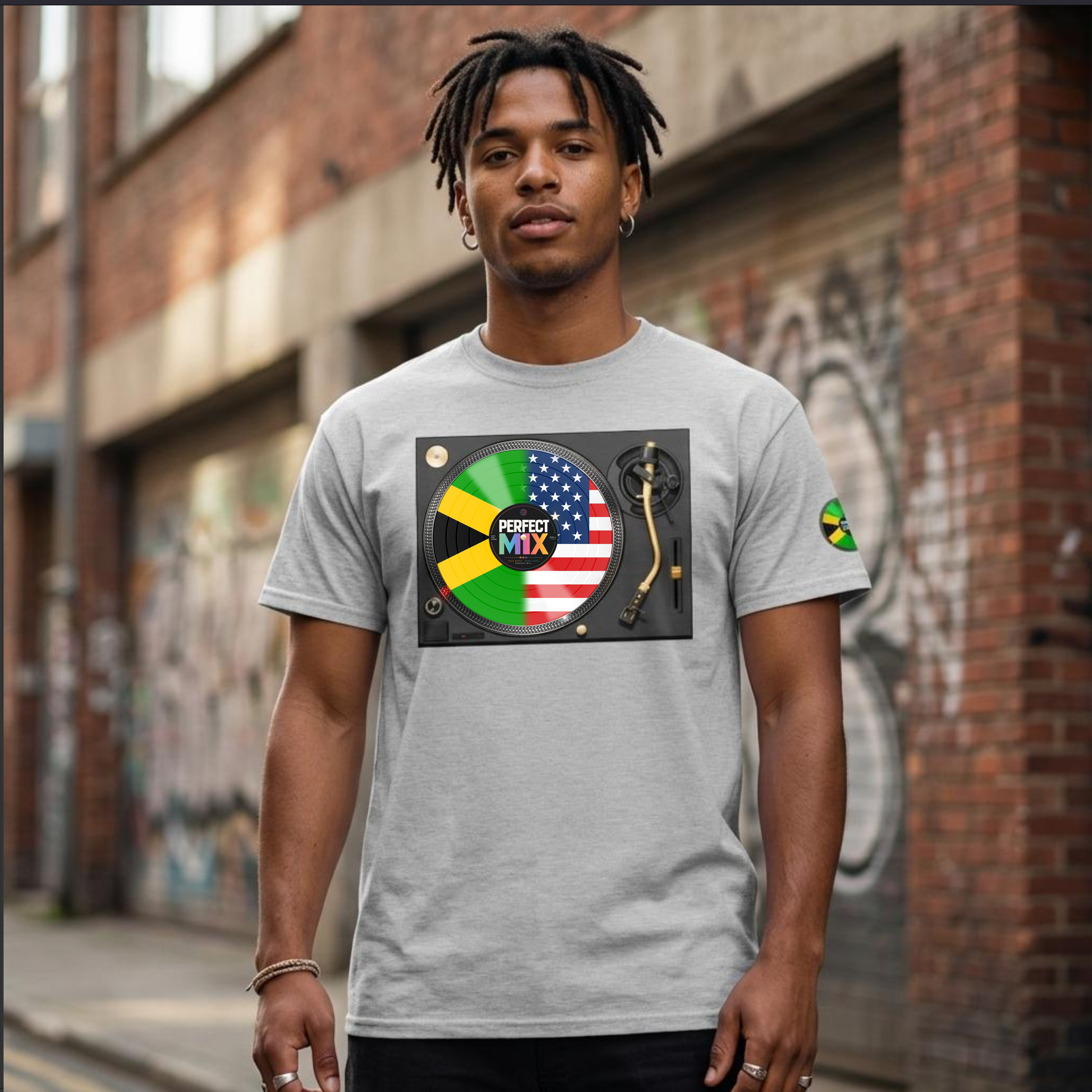 A mixed heritage man wearing a light gray t-shirt with a graphic print of a turntable featuring the Jamaican and USA flags and the text 'PERFECT MIX'. The background is an outdoor brick alleyway with graffiti.