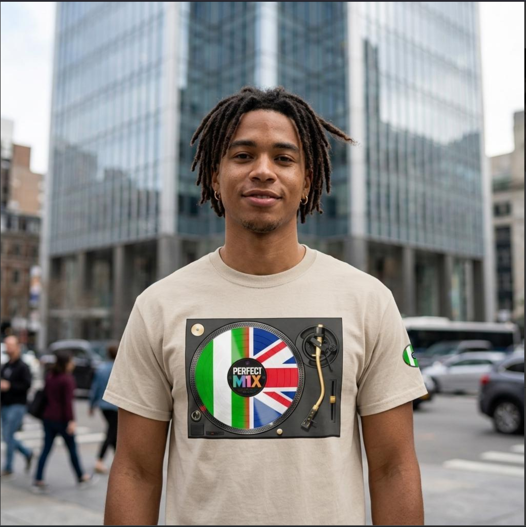 A man wearing a beige t-shirt with a graphic of a turntable playing a vinyl record decorated with the Nigerian and Union Jack flags and the words 'PERFECT MIX'. He is standing in a city street with modern glass skyscrapers in the background.